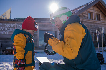 Image showing father preparing his little son for the first time on a snowboar