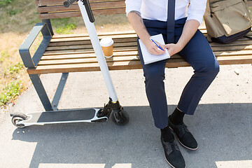 Image showing smiling businessman writing to notebook in city