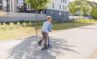 Image showing happy little boy riding scooter in city