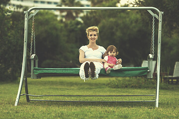 Image showing mother and little daughter swinging at backyard