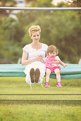 Image showing mother and little daughter swinging at backyard