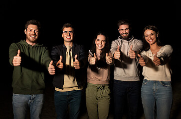 Image showing happy smiling friends showing thumbs up at night