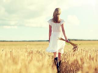 Image showing young woman with cereal spikelets walking on field