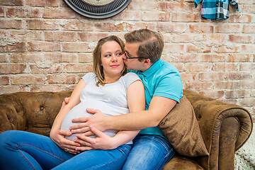 Image showing A man kissing his pregnant woman. A man kissing his pregnant woman. They are sitting.