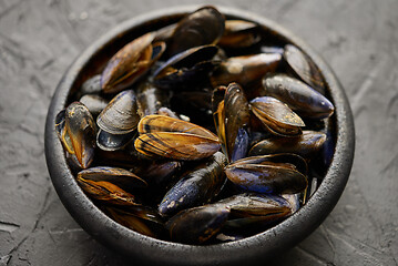 Image showing Fresh and raw sea mussels in black ceramic bowl placed on dark stone background