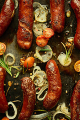 Image showing Tasty grilled homemade rosemary sausages placed on iron frying tray over rustic dark stone table