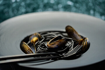 Image showing Seafood black spaghetti pasta with clams served on black plate on dark stone