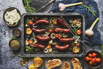 Image showing Top view on delicious grilled sausages served with onion, tomatoes, garlic, bread and herbs