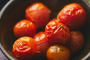 Image showing Roasted cherry Tomatoes placed in a ceramic dark bowl. Close up macro shot.