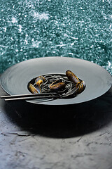 Image showing Seafood black spaghetti pasta with clams served on black plate on dark stone