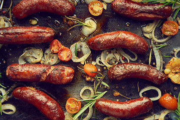 Image showing Top view on delicious grilled sausages served with onion, tomatoes, garlic, bread and herbs