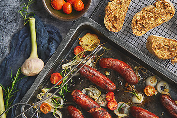 Image showing Tasty grilled homemade rosemary sausages placed on iron frying tray over rustic dark stone table