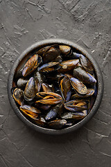 Image showing Fresh and raw sea mussels in black ceramic bowl placed on dark stone background