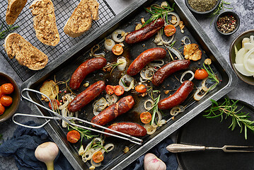 Image showing Top view on delicious grilled sausages served with onion, tomatoes, garlic, bread and herbs