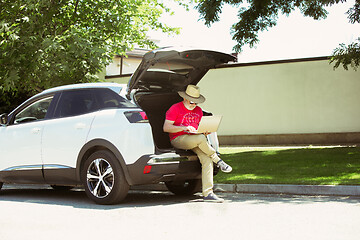 Image showing Senior man sitting on his car\'s trunk and working outdoors