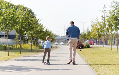 Image showing happy father and little son riding scooter in city