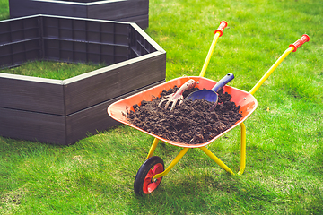 Image showing Garden barrow with soil and empty raised beds on grass prepared for filling with soil