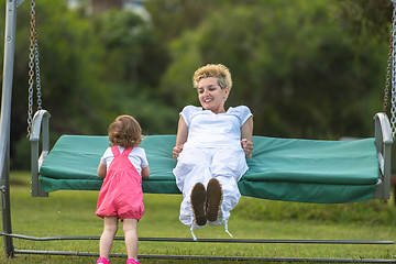 Image showing mother and little daughter swinging at backyard