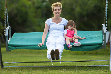 Image showing mother and little daughter swinging at backyard