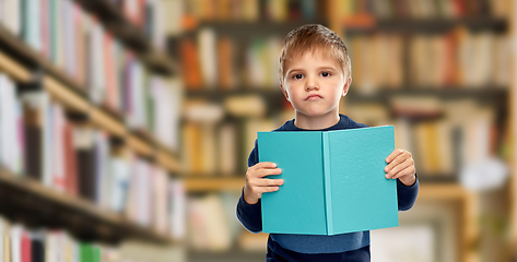 Image showing displeased little boy reading book over library