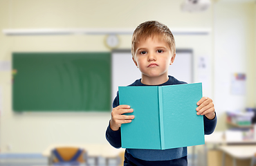 Image showing displeased little boy with book at school