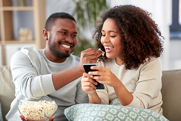 Image showing african couple with popcorn and smartphone at home