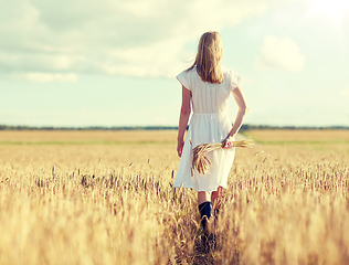 Image showing young woman with cereal spikelets walking on field