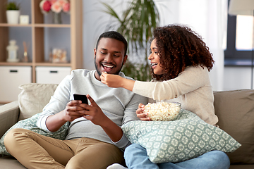 Image showing african couple with popcorn and smartphone at home