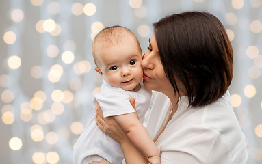 Image showing happy mother kissing little baby over lights