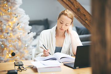 Image showing Young female entrepreneur wearing cosy warm bathrobe working remotly from home in winter Christmas time during 2020 corona virus pandemic. Work from home, selter in place, concept.