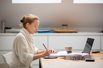 Image showing Young female entrepreneur wearing cosy warm bathrobe working remotly from home in winter Christmas time during 2020 corona virus pandemic. Work from home, selter in place, concept.