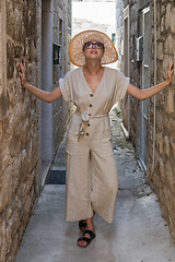 Image showing Beautiful blonde young female traveler wearing straw sun hat sightseeing and enjoying summer vacation in an old traditional costal town at Adriatic cost, Croatia.