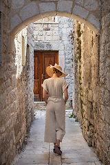 Image showing Rear view of beautiful blonde young female traveler wearing straw sun hat sightseeing and enjoying summer vacation in an old traditional costal town at Adriatic cost, Croatia