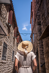 Image showing Rear view of beautiful blonde young female traveler wearing straw sun hat sightseeing and enjoying summer vacation in an old traditional costal town at Adriatic cost, Croatia