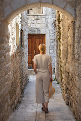 Image showing Rear view of beautiful blonde young female traveler wearing straw sun hat sightseeing and enjoying summer vacation in an old traditional costal town at Adriatic cost, Croatia