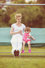 Image showing mother and little daughter swinging at backyard