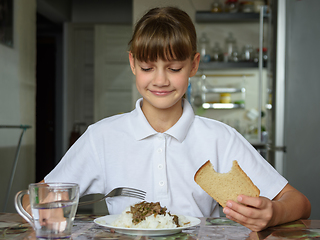 Image showing The girl is having dinner at the table, she looked at the food with appetite