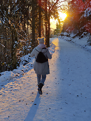 Image showing Woman hiking on snow in white winter forest berore the sunset. Recreation and healthy lifestyle outdoors in nature