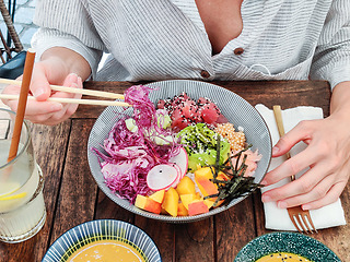 Image showing Woman eating tasty colorful healthy natural organic vegetarian Hawaiian poke bowl using asian chopsticks on rustic wooden table. Healthy natural organic eating concept