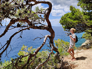 Image showing Young active feamle tourist wearing small backpack walking on coastal path among pine trees looking for remote cove to swim alone in peace on seaside in Croatia. Travel and adventure concept