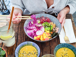 Image showing Woman eating tasty colorful healthy natural organic vegetarian Hawaiian poke bowl using asian chopsticks on rustic wooden table. Healthy natural organic eating concept