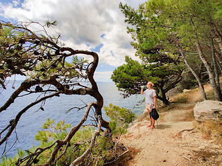 Image showing Young active feamle tourist taking a break, drinking water, wearing small backpack while walking on coastal path among pine trees looking for remote cove to swim alone in peace on seaside in Croatia