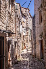 Image showing Rear view of beautiful blonde young female traveler wearing straw sun hat sightseeing and enjoying summer vacation in an old traditional costal town at Adriatic cost, Croatia