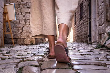 Image showing Detail shot of female legs wearing comfortable travel sandals walking on old medieval cobblestones street dring sightseeing city tour. Travel, tourism and adventure concept
