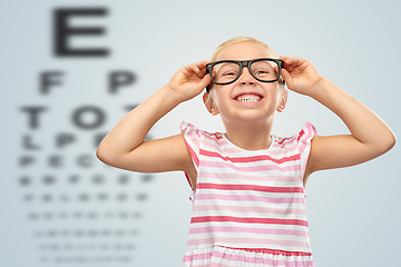 Image showing smiling little girl in glasses over eye test chart