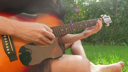 Image showing Man sitting in the grass playing guitar