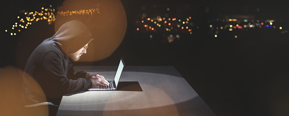 Image showing hacker using laptop computer while working in dark office