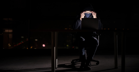 Image showing hacker using laptop computer while working in dark office