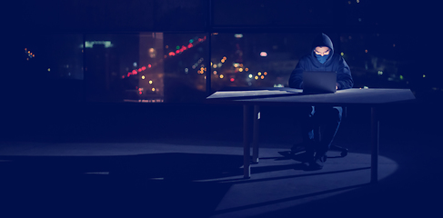 Image showing hacker using laptop computer while working in dark office