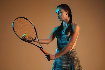 Image showing One caucasian woman playing tennis on brown background in mixed light